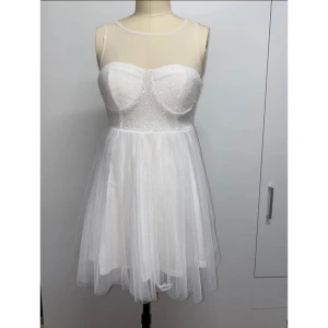 Vit axelbandslös klänning - Säljer en söt vit axelbandslös klänning med ett glittrigt liv och en luftig tyllkjol. Klänningen har en dragkedja i ryggen och en transparent meshdetalj upptill. Perfekt för sommarens fester eller studentfirandet! ✨