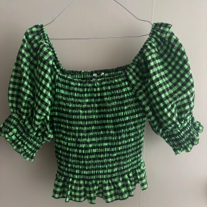 Grön och svart rutig Zara topp - Säljer en söt grön och svart rutig blus med puffiga kortärmar och smockdetaljer. Den har en elastisk passform och volangkant nedtill. Perfekt för en trendig look!