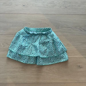 Blommig kortkjol i grönt - Söt kortkjol i grönt med ett blommigt mönster. Kjolen har volanger som ger en lekfull look. Perfekt för varma dagar! Shorts under.