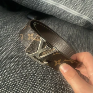 Brunt bälte från Louis Vuitton - Snyggt brunt bälte från Louis Vuitton med det klassiska monogrammönstret. Bältet har ett stort LV-spänne i silverfärg som ger en lyxig touch. Perfekt för att lyfta vilken outfit som helst. !äkta! 