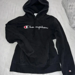 Svart hoodie från Champion - Säljer en svart hoodie från Champion med det klassiska logotypen broderad på bröstet. Tröjan har en bekväm passform med långa ärmar och en praktisk ficka framtill. Perfekt för en avslappnad stil. Storlek Medium