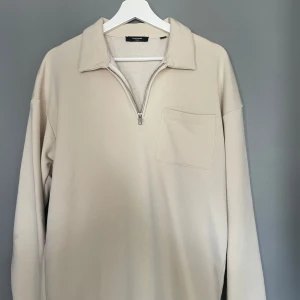 Beige tröja med dragkedja från Jack & Jones - Säljer en stilren beige tröja från Jack & Jones med dragkedja och krage. Tröjan har en bröstficka och långa ärmar, perfekt för en avslappnad look. Passar bra till både jeans och chinos.