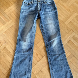 Blå bootcut jeans - Snygga blå bootcut jeans med klassisk femficksdesign och låg midja. Perfekta för en avslappnad stil med en touch av retro. De har en lätt tvättad look som ger en cool vibe.
