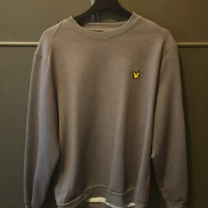 Grå sweatshirt från Lyle & Scott - Säljer en stilren grå sweatshirt från Lyle & Scott med deras ikoniska logga på bröstet. Tröjan har långa ärmar och ribbade muddar vid ärmslut och nederkant. Perfekt för en avslappnad look. Pris går att prata om