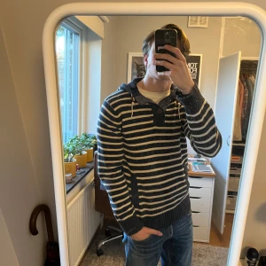 Unik randig stickad hoodie - Säljer en snygg och väldigt unik randig stickad hoodie i marinblått och vit. Tröjan har riktigt schyssta detaljer med knapparna och snörena! Den är i bra skick, inga fläckar eller hål, och är riktigt skön. Perfekt till svala sommarkvällar!🤩 Skriv vid frågor eller prisförslag!