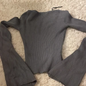 Grå ribbad tröja - Säljer en stilren grå ribbad tröja med lång ärm och v-ringning. Perfekt för en avslappnad men ändå elegant look. Tröjan har en figurnära passform och är tillverkad i ett mjukt material.