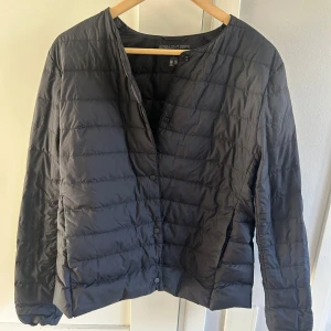 Svart dunjacka från Uniqlo - Säljer en stilren svart dunjacka från Uniqlo. Jackan har en quiltad design med knappar framtill och långa ärmar. Perfekt för kyligare dagar och lätt att matcha med olika outfits.