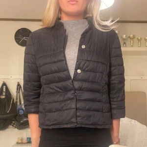 Svart herno liknande jacka  - Snygg svart quiltad jacka med trekvartsärm och knappar. Perfekt för höst och vår. Jackan har en stilren design och är lätt att matcha med olika outfits. Obs, lånade bilder