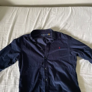 Mörkblå machester skjorta från Polo Ralph Lauren - Säljer en stilren mörkblå skjorta från Ralph Lauren i slim fit. Skjortan är i manchester och passar perfekt till våren/sommaren. Kan användas på egen hand men även som en overshirt med en tshirt under. 