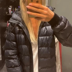 Svart dunjacka från Peak Performance - Säljer en svart/ mörkblå , puffig dunjacka från Peak Performance med huva och dragkedja framtill. Jackan har quiltad design och ribbade muddar vid ärmsluten. Perfekt för kalla dagar och har en snygg, oversized look. Passar dig som gillar streetstyle och vill hålla dig varm.