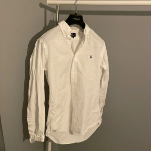 Vit skjorta från Polo Ralph Lauren - Vit klassisk skjorta från Polo Ralph Lauren i custom fit. Skjortan har lång ärm, knappar framtill och den ikoniska broderade loggan på bröstet. Tillverkad i mjuk bomull och har en stilren krage. Perfekt för dig som gillar enkel och snygg stil. Hör av er vid fu deri gar🤗