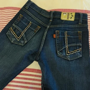Blå jeans med broderade fickor - Säljer ett par mörkblå jeans med snygga broderade detaljer på bakfickorna. Bootcut passform. Storlek 29, vet tyvärr inte långt men passar mig som är 170cm. Knappt använd. 