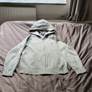 Ralph lauren Hoodie Grå (zip) - Säljer denna snygga Ralph lauren zip i ett bra skick, använd men fortfarande bra omhändertagen. Storlek 14-16 = XS/S. Jag är ungefär 164 och den passar mig men på gränsen. Nypris 1095, så 500 är bra pris💸Hör av er vid funderingar Mvh Max