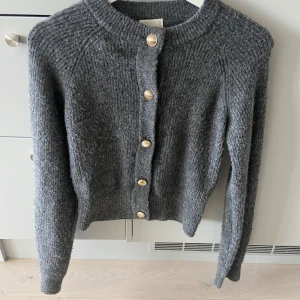 Mörkgrå stickad kofta - Säljer en mörkgrå stickad kofta från H&M i storlek XS. Koftan har rund hals, långa ärmar och snygga guldfärgade knappar framtill. Perfekt att slänga på sig när det är kyligt ute. Materialet är mjukt och ger en mysig känsla nu till hösten🩶