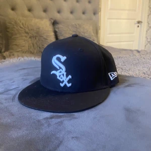 Svart New Era White Sox keps (snapback) profil för mer - Säljer en svart snapback keps från New Era, modell 9FIFTY, med White Sox-logga broderad i vitt framtill. Kepsen har platt skärm och justerbar baksida med plastspänne. Klassisk streetstil och perfekt för dig som gillar baseball eller sportiga accessoarer.