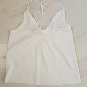 Vit ribbad linnetopp med smala band - Supersnygg vit linnetopp med smala axelband och v-ringad front. Toppen är ribbad och har en mjuk, stickad känsla som gör den perfekt för varma dagar. Enkel och clean design som är lätt att matcha med jeans eller kjol. Perfekt för dig som gillar minimalistisk stil.