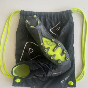 Nike Air Zoom Mercurial fotbollsskor - Nike Air Zoom Mercurial fotbollsskor i svart med neon-gula detaljer och sula. Skorna har snörning, rund tå och är tillverkade i syntetmaterial med stickad ovandel för extra komfort. Perfekta för dig som vill ha grymt grepp och respons på planen.