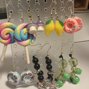Färgglada örhängen med roliga motiv - Unika örhängen med motiv som klubbor i pastellfärger, svampar i lila, rött och gult, citroner, donuts, giraffer, persikor, svarta pärlor med stjärnor och gröna kiwi-skivor. Perfekt för dig som vill sticka ut med lekfull och kreativ stil.