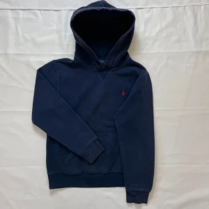 Mörkblå hoodie från Polo Ralph Lauren - Snygg mörkblå hoodie från Polo Ralph Lauren med klassiska logotypen i rött, storlek L (14-16) Barn, vilket motsvarar en S i vuxenstorlek! | Skick: 9 / 10, väldigt bra skick! | Nypris: 2300 | Vårt pris: 899 | Storlek: S | Tveka inte att höra av er med bud eller funderingar!