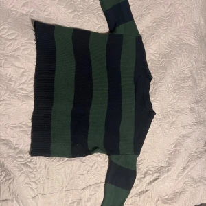 Randig stickad tröja i grönt och svart - Säljer en chill stickad tröja med breda gröna och svarta ränder. Tröjan har rund hals och långa ärmar, perfekt för att hålla sig varm. Ribbstickad vid muddar och nederkant för extra comfy känsla. Passar dig som gillar klassisk streetstyle.