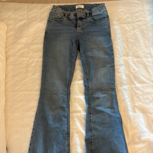 Blå bootcut jeans från Lindex, stl 164 - Snygga blå bootcut jeans från Lindex i storlek 164. Jeansen har coola bakfickor med stjärnbroderi och kontrastsömmar, samt justerbar midja med resår. 