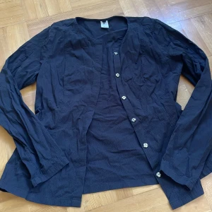 Marinblå kofta från Visual Clothing Project - Snygg marinblå kofta från Visual Clothing Project i storlek S. Koftan har ett tunt, krinklat tyg och dekorativa blommiga knappar framtill. Långärmad och perfekt att slänga över en t-shirt eller linne för en chill look.