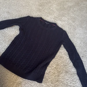 Mörkblå stickad tröja Tommy Hilfiger - Snygg mörkblå stickad tröja från Tommy Hilfiger i storlek XS. Tröjan har ett klassiskt kabelstickat mönster, rund hals och långa ärmar. Perfekt för dig som gillar stilrena och tidlösa plagg med en preppy vibe. Original pris 1700 men jag säljer för 950