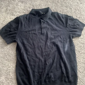 Svart pikétröja från J.Lindeberg - Mörkblå pikétröja från J.Lindeberg med klassisk krage och två knappar framtill. Tröjan har korta ärmar och diskret broderad logga på bröstet. Mjuk och skön bomullskvalitet som passar perfekt till jeans eller shorts. 