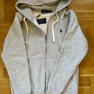 Grå hoodie från Polo Ralph Lauren - Har ingen användning enda sen jag köpte den, helt ny aldrig haft på mig sen ute bara testat inomhus. OBS: Kom med bud så kan vi förhandla!