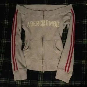 grå kofta  - Säljer  gråa zip up kofta som har tryck och 2 röda sträck på armarna. Storlek S  köpte den från plick men tyvärr var inte min size