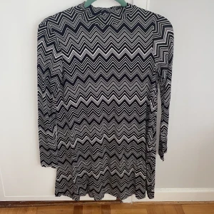 Svartvit zigzag klänning Gina Tricot - Cool svartvit klänning från Gina Tricot i storlek S med ett grafiskt zigzag-mönster. Klänningen har lång ärm, hög hals och är i kort modell. Perfekt för dig som gillar att sticka ut med mönster och vill ha en bekväm och snygg look.