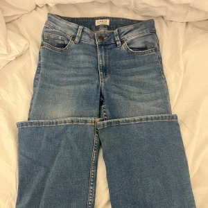 Blå jeans från Lindex, storlek 34 - Snygga ljusblå jeans från Lindex med klassisk femficksdesign och bruna detaljer vid knappar och nitar. Modellen har raka ben och normal passform, tillverkade i mjukt bomullsjeansmaterial. Perfekt för dig som gillar en enkel och clean look.