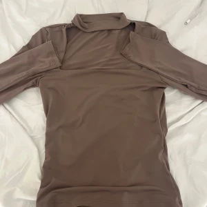 Beige polotröja med cut out från NA-KD - Säljer en beige polotröja från NA-KD i storlek XS. Tröjan har lång ärm och cool cut out-detalj vid axlarna som ger en edgy vibe. Materialet är mjukt och stretchigt, perfekt för layering eller att bära som den är. Passar dig som gillar trendiga och unika plagg.