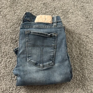 Blå jeans från Tiger of Sweden 31/32 - Snygga blå jeans från Tiger of Sweden i klassisk denim. Modellen har fem fickor, bälteshällor och knappstängning. Jeansen har en rak passform som ger en avslappnad vibe. Perfekt för dig som gillar stilrena och tidlösa jeans.