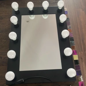 Svart sminkspegel med LED-lampor - Stor rektangulär sminkspegel med svart ram och 12 runda LED-lampor runt kanten för perfekt belysning när du sminkar dig. Spegeln har sladd för elanslutning och är perfekt för att få till detaljerna i din makeup. Snygg och modern design. Speglen är i mått 70x50, orginal priset på spegeln va 1500 ❤️