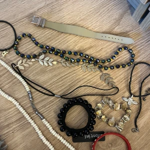 Mixade halsband och armband med pärlor - Samling med flera smycken: två halsband med vita och svarta pärlor, ett färgglatt hårband med blad i guld, ett armband med svarta pärlor, ett armband med guldfärgade stenar och ett rött plastarmband. Perfekt för dig som gillar att variera din stil.