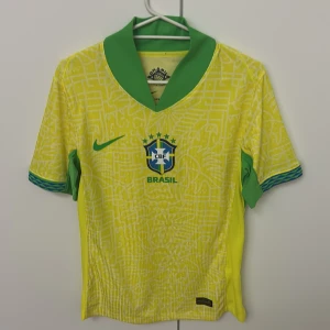 Brasilien Nike fotbollströja gul/grön - Säljer en officiell Brasilien fotbollströja från Nike med gul bas och gröna detaljer. Tröjan har korta ärmar, grönt krage och ett unikt grafiskt mönster över hela tyget. Materialet är Dri-FIT ADV för extra komfort och ventilation. Perfekt för dig som älskar fotboll och vill sticka ut.