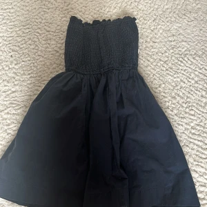 Svart kort klänning från Hollister XS - Supersöt svart klänning från Hollister i storlek XS. Klänningen är axelbandslös med smockad överdel och utställd kjol. Liten broderad Hollister-logga i rött vid nederkanten. Perfekt för varma dagar!