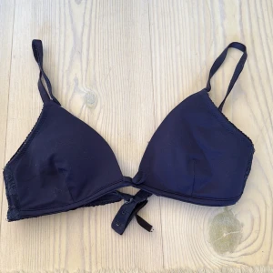 Mörkblå bh från Lindex - Snygg mörkblå bhöverdel från Lindex med trekantsformade kupor och justerbara axelband. Sidorna har spetsdetaljer och framtill finns en liten rosett. Stängs med hakar i ryggen. 