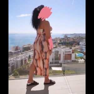 Mönstrad axelbandslös långklänning - Säljer en snygg axelbandslös långklänning med ett coolt mönster i beige, svart och orange toner. Klänningen har en flowy passform och slits på sidan, perfekt för varma dagar. Materialet känns lätt och luftigt, vilket gör den superbekväm att bära.