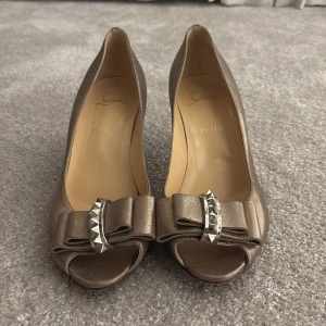 Guldiga pumps från Christian Louboutin - Snygga guldiga pumps från Christian Louboutin med klassisk röd sula, spetsig klack och öppen tå. Måste klackas om. Skorna är lite slitna på undersidan från gatorna på stan. Annars är det nästan igen damige