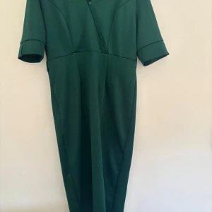 Mörkgrön långklänning med bälte - Snygg mörkgrön långklänning med korta ärmar. Klänningen har ett matchande bälte med silverfärgade knappar.