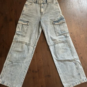 Wide cargo jeans från H&M, ljusblå - Säljer ett par ljusblå wide cargo jeans. Byxorna har breda ben, stora cargofickor på sidorna och klassisk femficksdesign. Tillverkade i 100% bomull för en skön och avslappnad känsla. Perfekt för dig som gillar streetwear och loose fit.