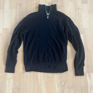 Svart stickad polotröja med half zip - Svart stickad polotröja från Jack and Jones med half zip i halsen. Tröjan har långärmade ribbade muddar och en hög krage som går att öppna med dragkedja. Perfekt för dig som gillar stilrena och klassiska plagg med en modern touch.