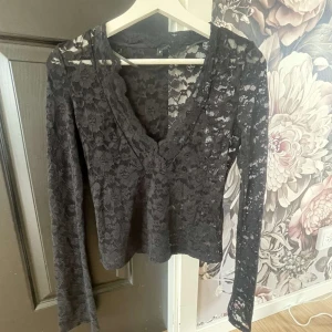 Svart spetsblus från Vero Moda XS - Svart långärmad blus från Vero Moda i storlek XS. Blusen är helgjord i transparent spets med blommigt mönster och har en snygg v-ringad halsringning med vågig kant. Använt upp till 1-2 gånger.