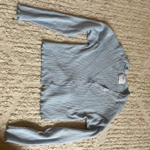 Ljusblå ribbad kofta från Zara - Säljer en ljusblå ribbad kofta från Zara med v-ringning och knappar framtill. Koftan har långa ärmar och är gjord i ett mjukt, stretchigt material som sitter snyggt på kroppen. Aldrig använd 