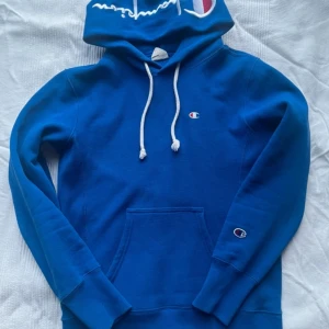 Blå Champion hoodie XS - Säljer en blå hoodie från Champion i storlek XS. Tröjan har vit snörning i huvan, klassisk känguruficka och Champion-logga broderad på bröstet och ärmen. Reverse Weave-materialet gör den extra mjuk och skön. Perfekt för chill eller streetwear.