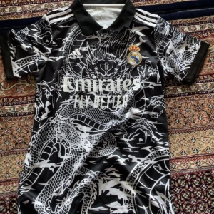 Real Madrid fotbollströja - Snygg Real Madrid fotbollströja från Adidas i svart med vit drakmönster över hela tröjan. Klassisk krage, korta ärmar och broderat klubbmärke på bröstet. Materialet är lätt och andas, perfekt för träning eller häng. Emirates sponsortryck på framsidan. Direkt från Spanien 