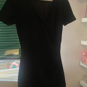 Svart omlottklänning med kort ärm - Säljer en svart omlottklänning med kort ärm och v-ringning. Klänningen har en figurnära passform och är perfekt för dig som gillar en stilren look. Enkel att styla med accessoarer för olika tillfällen.