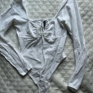 Vit långärmad bodysuit från H&M - Säljer en stilren vit långärmad bodysuit från H&M. Den har en snygg knytdetalj framtill och är perfekt för lager-på-lager. Passar både till jeans och kjol. Perfekt basplagg för garderoben! Aldrig använd🦋😍